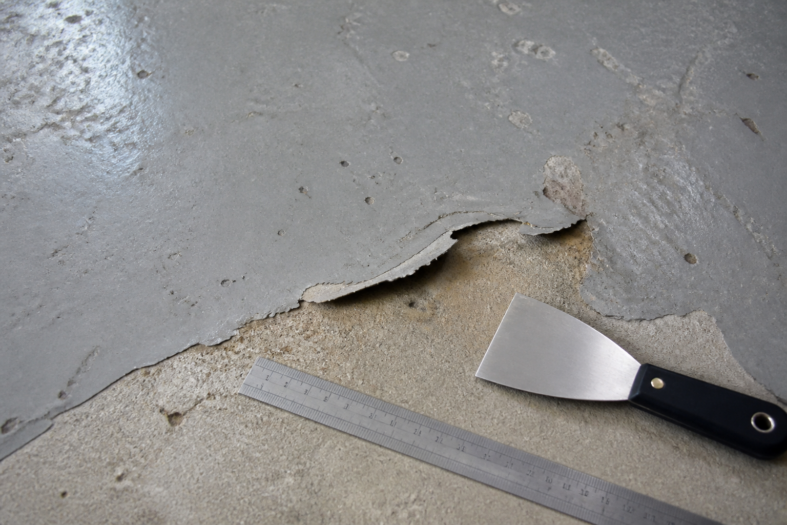 Worn garage coating lifting from the concrete during an assessment